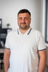 Ein Mann mit kurzem Bart und weißem Poloshirt lächelt in die Kamera.