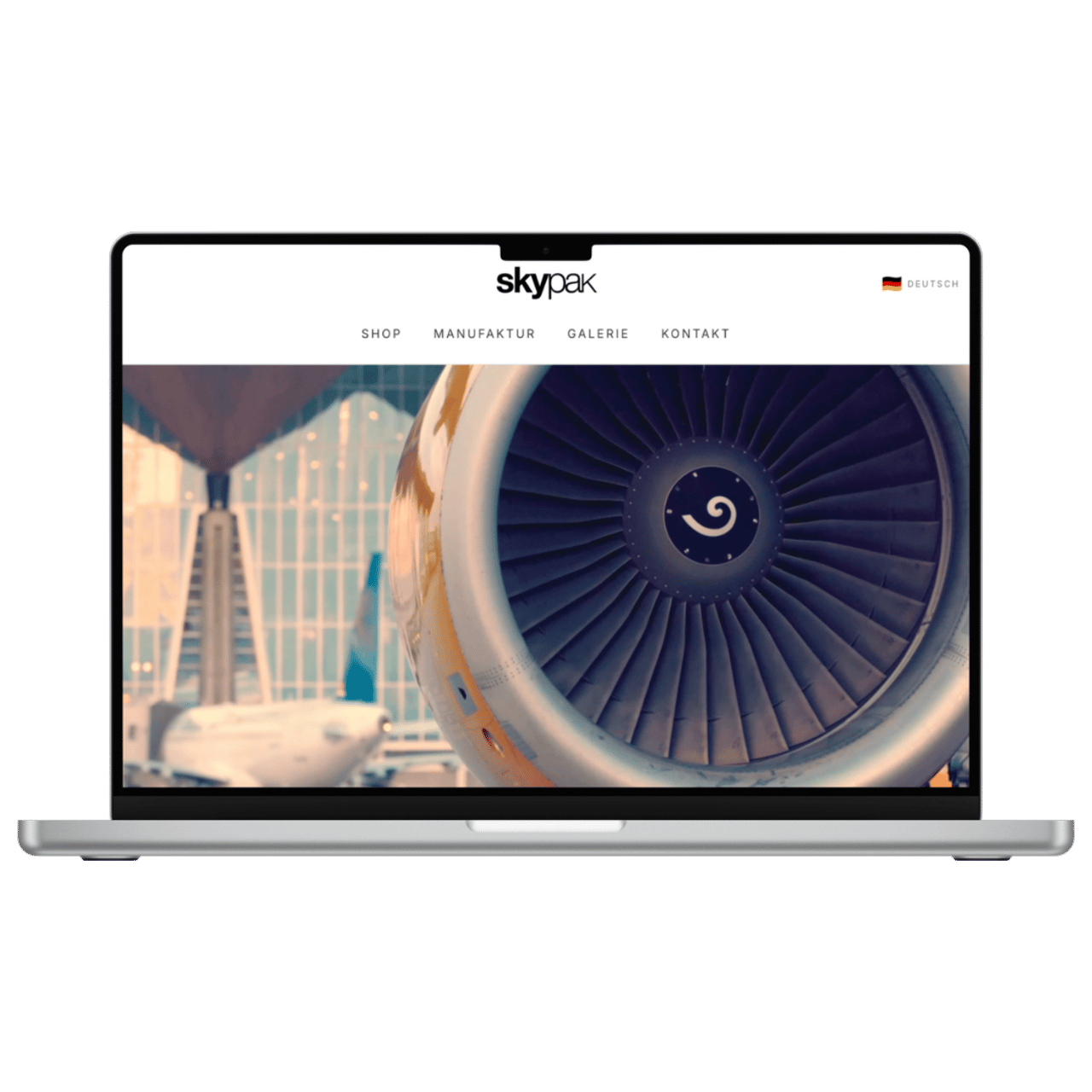 Laptop zeigt SkyPak-Website mit Flugzeugtriebwerk und Text "SHOP MANUFAKTUR GALERIE KONTAKT".