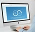 Eine Person tippt an einem iMac-Computer, der eine Webseite mit blauen Kreisen und Pfeilen anzeigt.