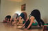 Vier Frauen praktizieren die Yoga-Übung herabschauender Hund auf Matten in einem hellen Studio.