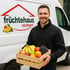 Mann hält eine Obstkiste vor einem Lieferwagen mit dem Logo "früchtehaus stuttgart" und Früchten.