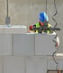 A construction worker in a blue hard hat and safety vest uses a mechanical hoist to lay large white concrete blocks.