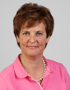 Frau mit kurzen braunen Haaren, rosa Polohemd und Perlenkette blickt nach vorne.