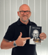 Uwe Bothe hält ein Buch mit seinem Porträt und dem Titel "S.O.S." in den Händen.