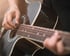 Eine Person spielt eine schwarze Akustikgitarre mit der rechten Hand über den Saiten.