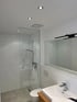 Modernes Badezimmer mit Glasdusche, WC und Waschbecken mit Holzunterschrank.