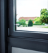 Kleiner weißer Alarmsensor am Rahmen eines modernen, dunkelgrauen Fensters mit Blick ins Grüne.