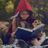 Young girl in red hood reading a book with stuffed animals in a forest.