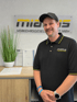 Lächelnder Mann in schwarzem Polo-Shirt und Kappe vor einem "miabus" Logo und Urkunden.