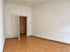 Leeres Zimmer mit weißen Wänden, hellem Laminatboden und einer offenstehenden weißen Innentür.