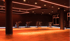 Dunkler Fitnessraum mit orangefarbener Beleuchtung, sechs Indoor-Cycling-Bikes und Fenstern.
