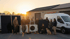 Ein Team von Handwerkern steht bei Sonnenuntergang mit Wärmepumpen, Solarmodulen und einem weißen Transporter vor einer Halle.