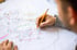Person zeichnet mit Bleistift auf einem detaillierten Bauplan mit bunten Markierungen.
