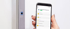 Eine Hand hält ein Smartphone mit der "easy dLine Fingerprint"-App neben einem grauen Türrahmen mit Fingerabdrucksensor.