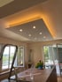 Deckenbeleuchtung mit gelben LED-Lichtbändern und integrierten Strahlern in einem Raum.
