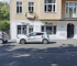 Weißes Auto mit "Violett" Logo parkt vor einem Gebäude mit "Violett" Geschäften.