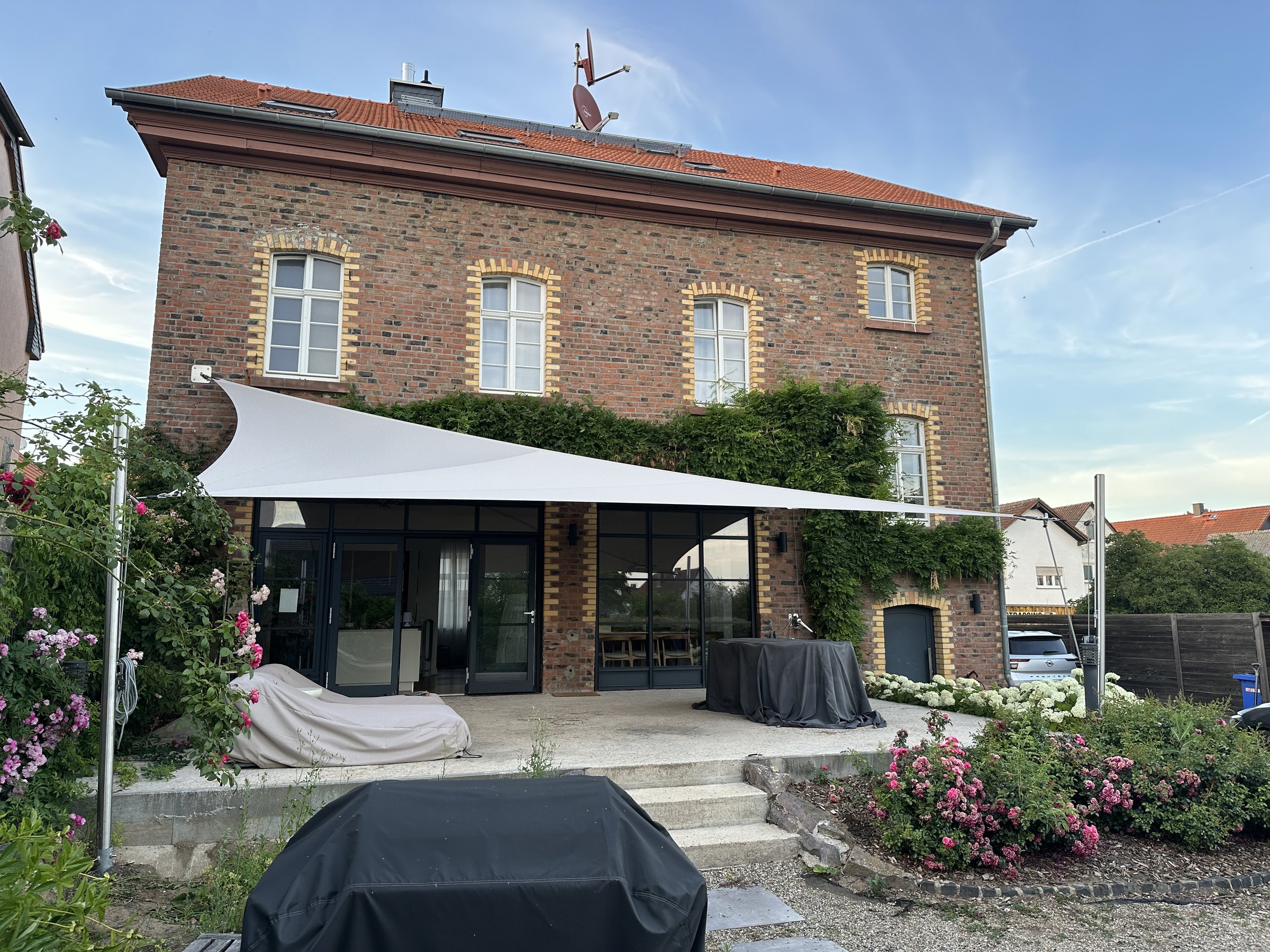 Das Backsteinhaus von vorne, mit fest verspanntem Sonnensegel über der Terrasse