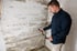 Ein Gutachter misst mit einem Feuchtigkeitsmessgerät die Feuchtigkeit an einer sanierungsbedürftigen Kellerwand aus Beton.