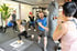Fünf Personen trainieren in einem Fitnessstudio, eine schlägt einen Boxsack, eine macht Ausfallschritte.