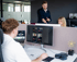Drei Kollegen arbeiten in einem modernen Büro; einer sitzt am Computer, während zwei andere stehen und etwas auf einem Bildschirm betrachten.