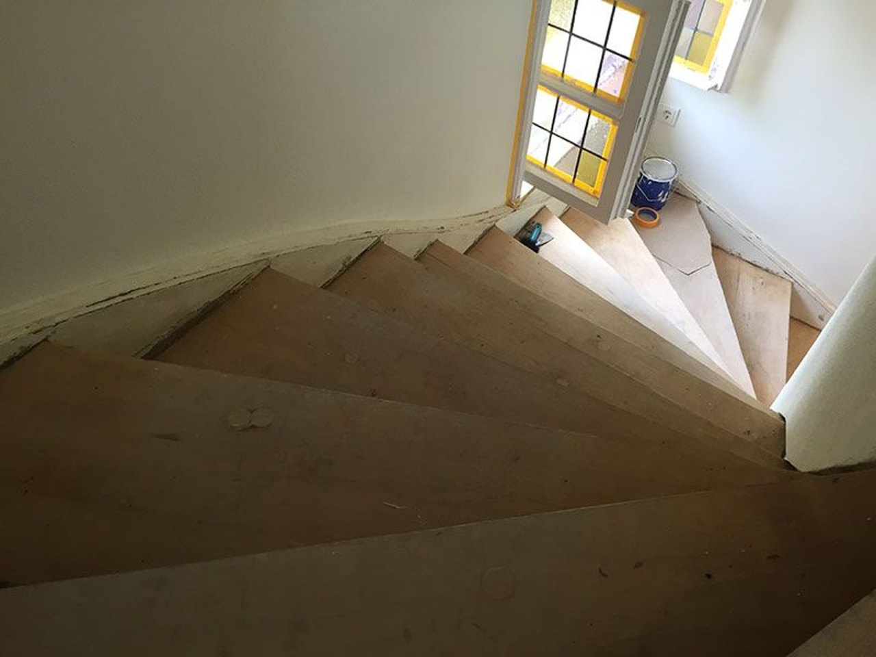 Blick von oben auf eine gewendelte Holztreppe während Renovierungsarbeiten mit Farbdose im Hintergrund.