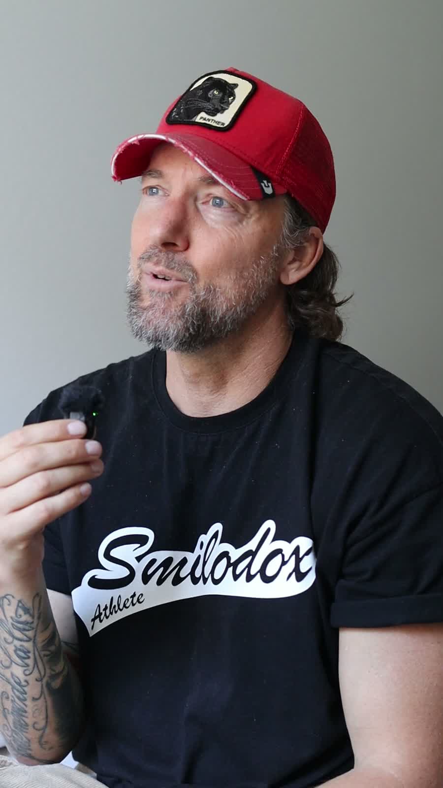 Patrick Maldinger im Interview mit Mikrofon, schwarzem T-Shirt und roter Kappe