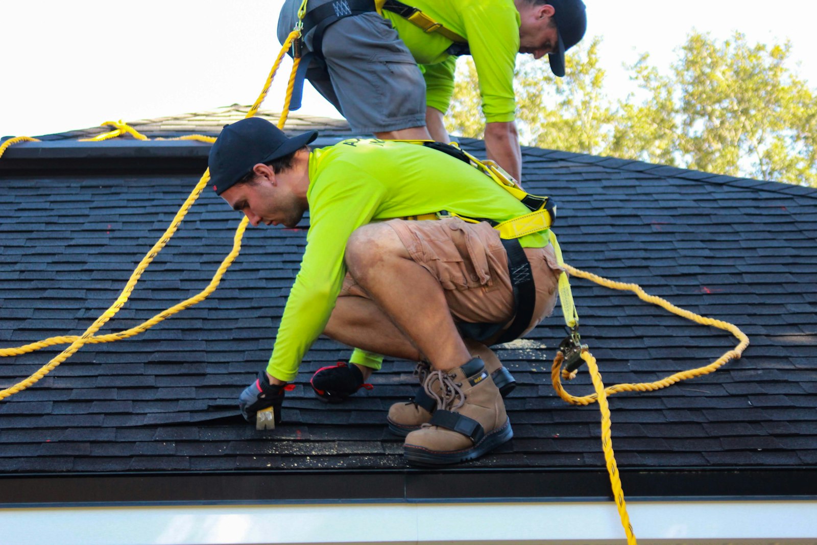Two roofers installing shingles on a pitched residential roof