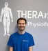 Ein lächelnder Mann in einem blauen T-Shirt mit „THERAmove“-Logo steht vor einer grauen Wand mit einer menschlichen Figur und dem Text „THERAmove Physiother“.