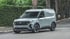 Grauer Ford Transit Courier Kastenwagen fährt auf einer Straße mit Bäumen und Büschen im Hintergrund.
