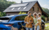 Familie steht vor einem Elektroauto, das vor einem Haus mit Solardach lädt.