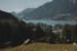 Blick über einen ruhigen See mit einem Dorf am Ufer und Bergen im Hintergrund.