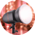 Studioblitz mit orangefarbenen Akzenten und Diffusor auf einem Stativ, Hintergrund mit Bokeh-Effekt.