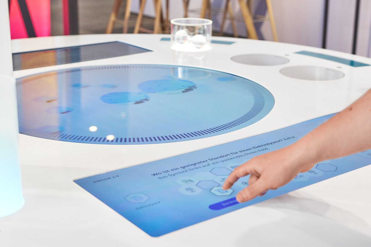 Interaktiver Experimentiertisch der Fraunhofer-Wanderausstellung: Besucherinnen und Besucher bestimmen per Multitouch den optimalen Standort für einen Elektrolyseur – spielerisch und wissenschaftlich fundiert.