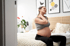 Pregnant woman on bed, easing neck and shoulder with prenatal care.