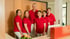 Sechs lächelnde Zahnarztpraxis-Mitarbeiter in roten Poloshirts stehen hinter einer Rezeption.