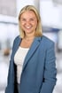 Lachende junge blonde Frau im blauen Blazer und weißem Oberteil.