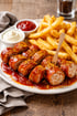 Currywurst mit Pommes Frites, Mayonnaise und Ketchup auf einem weißen Teller.