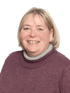 Ältere Frau mit blondem Haar und dunkelrotem Pullover, die lächelt.