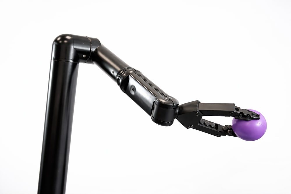 iARM: schwarzer Roboterarm mit Greifer, der eine violette Kugel hält