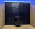 Eine schwarze, glänzende Toilette hängt vor einer Wand aus dunklen Ziegeln, beleuchtet von blauem LED-Licht.