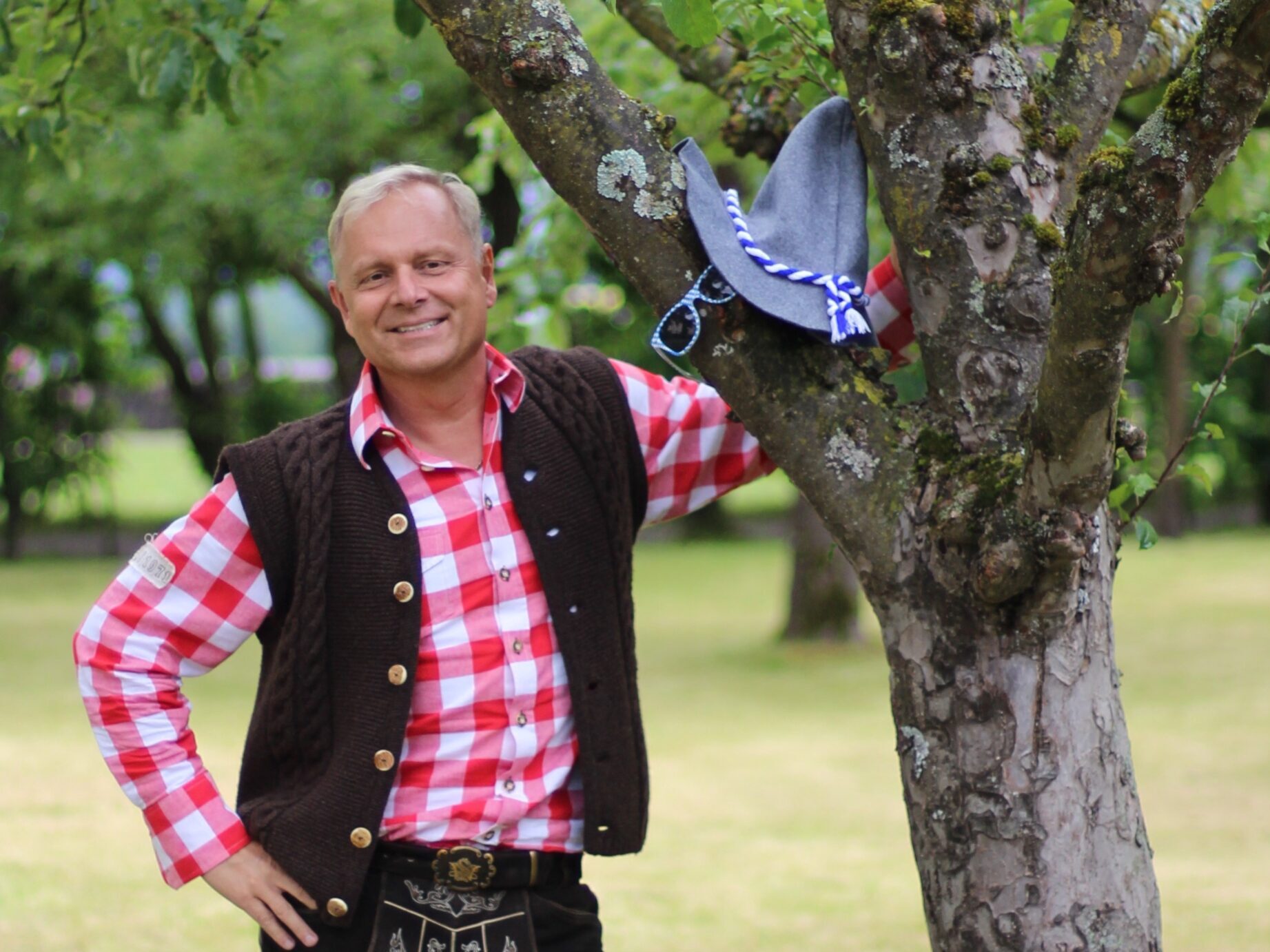 Uwe Rieder, der bayerische Vertriebsfreak — in bayerischer Tracht vor Baum stehend