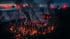 Zwei Drohnen mit roten und blauen Lichtern fliegen über einen Waldbrand mit brennenden Bäumen und einem zerfallenen Gebäude in der Nacht.