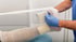 Pflegekraft in blauer Kleidung und Handschuhen legt einen Kompressionsverband am Unterschenkel eines Patienten an.