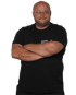 Ein Mann mit Brille und schwarzem T-Shirt mit der Aufschrift „S. SAUER SERVICETECHNIKER“ verschränkt die Arme.
