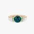 Goldener Ring mit einem großen blauen Saphir, umrahmt von hellgrünen und klaren Edelsteinen auf weißem Hintergrund.