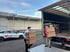 Zwei Umzugshelfer tragen bepackte Kartons vom Lkw-Laderampenbereich in Firmenhof