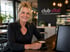 Lächelnde Frau mit blonden Haaren und schwarzem Oberteil hält eine Kaffeetasse vor einem "club vital" Logo.