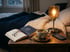 Kräutertee, Buch und Lesebrille auf dem Nachttisch im warmen Licht einer Lampe