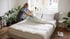 Reinigungskraft bezieht ein Bett in einem hellen, modern eingerichteten Apartment mit Pflanzen und Tageslicht