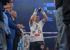 Ein Boxer in weißem T-Shirt und schwarzen Shorts mit erhobenen Händen und blauen Handschuhen im Ring.